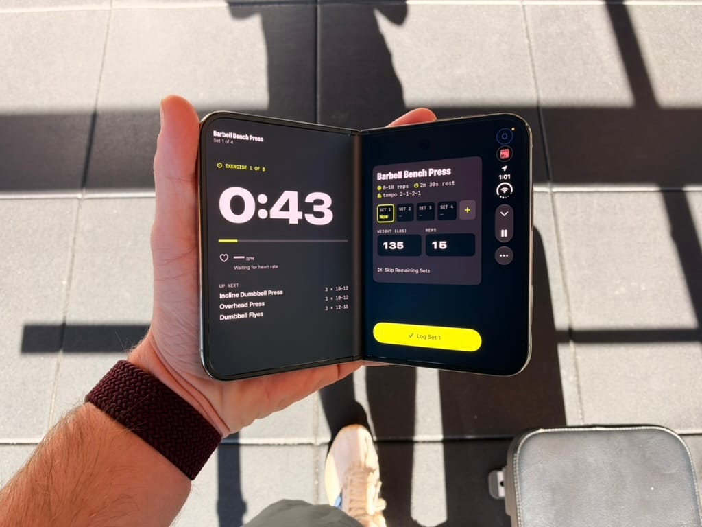 An unfolded iPhone Duo held in one hand, showing a workout app across its display.