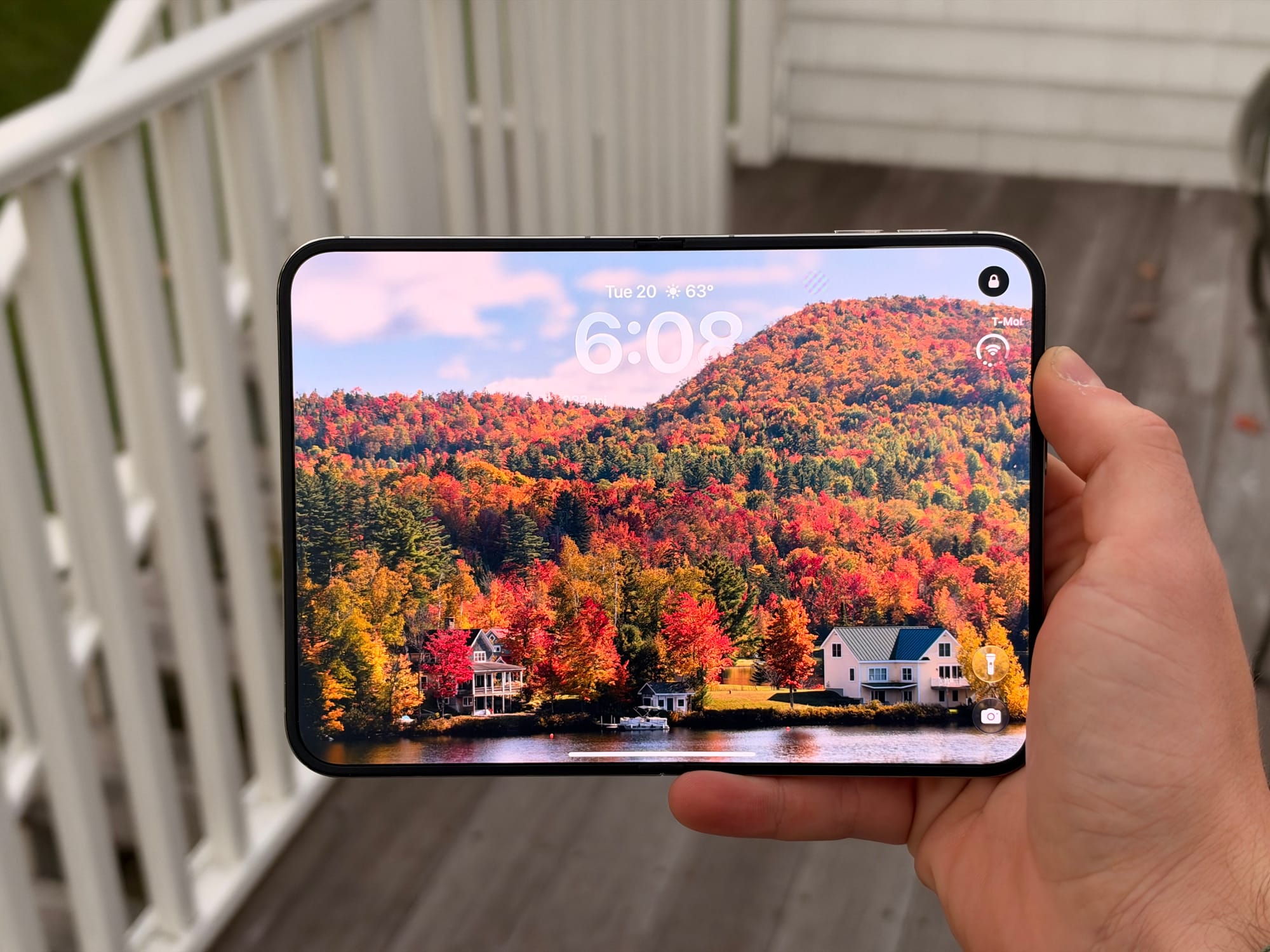 An unfolded iPhone Duo held outdoors, displaying a lock screen with autumn foliage.